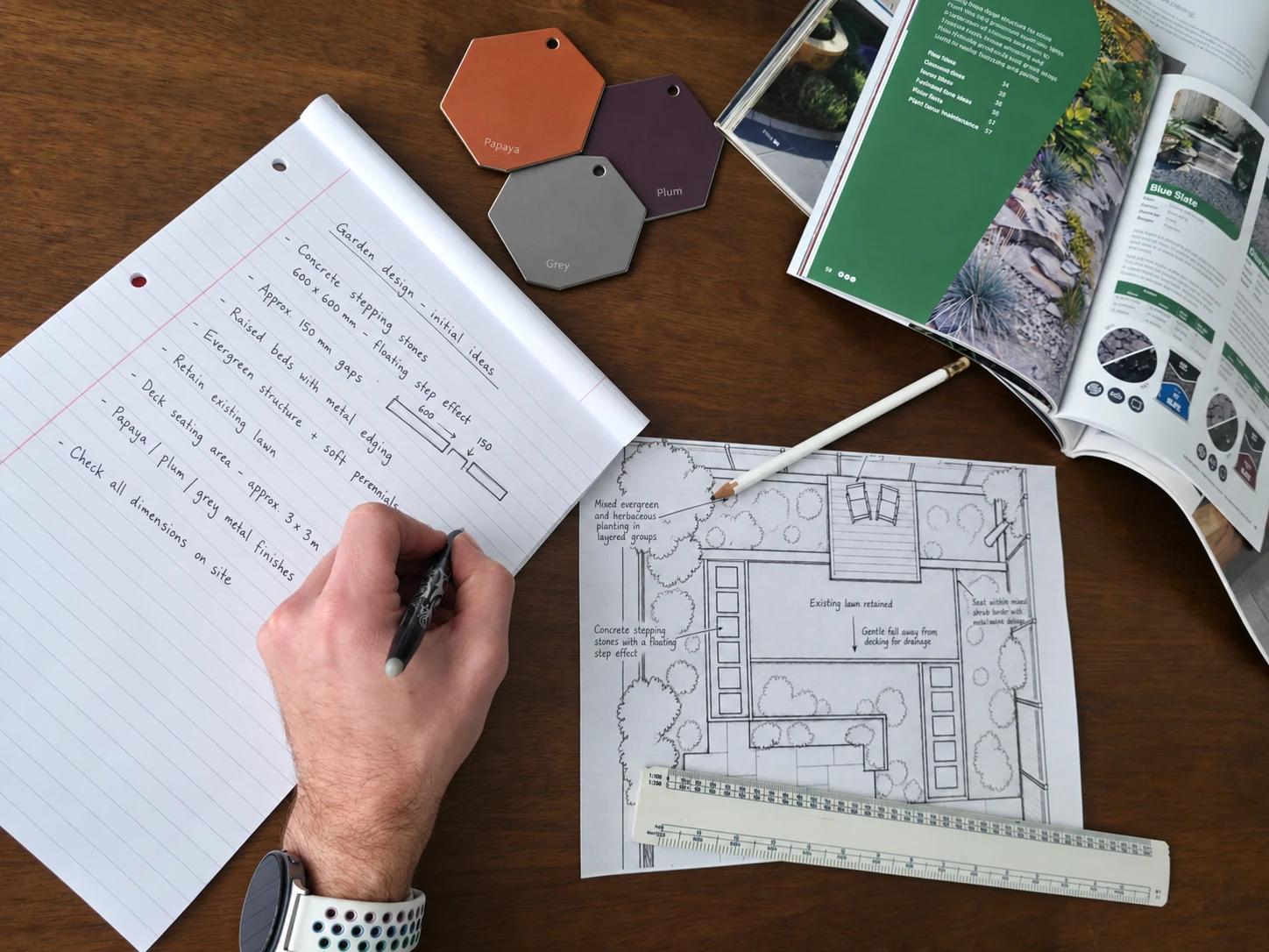 Garden design notes, an annotated plan and papaya, plum and grey material samples arranged on a wooden table